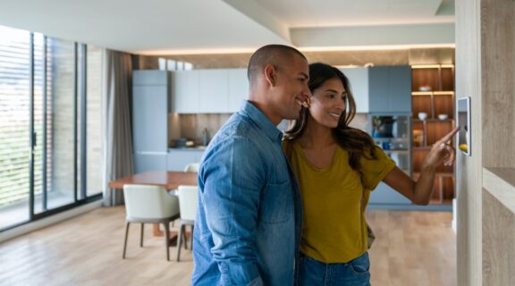 Photo of a female and male couple in their home using a touch screen device on their wooden wall